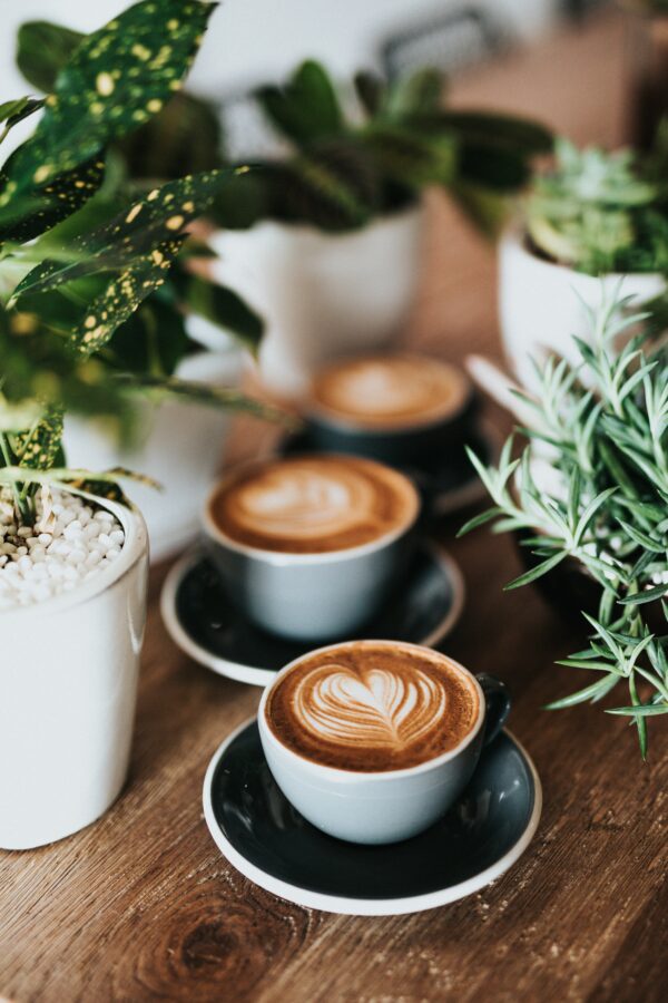 3 lattes in white cups on a wooden table with latte art in the shape of a heart on top..